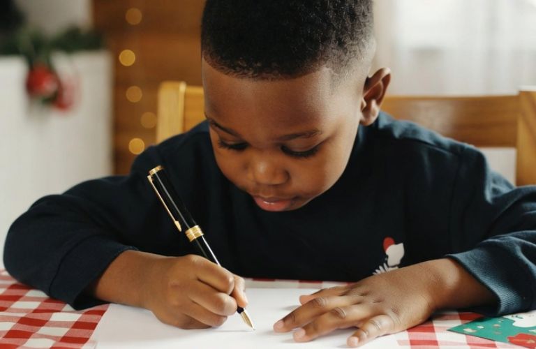 Child writing Christmas thank you letters with stationery and cards on festive table - Grok Imagine