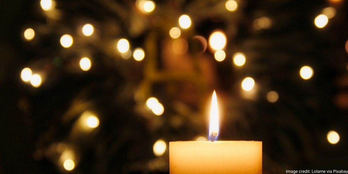 An image of a candle which has been lit on a backdrop that has fairy lights.